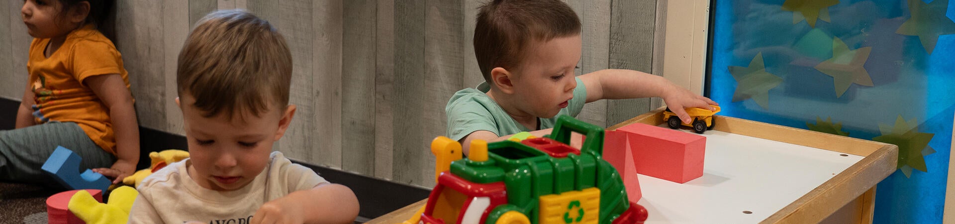 two toddlers playing with cars at table