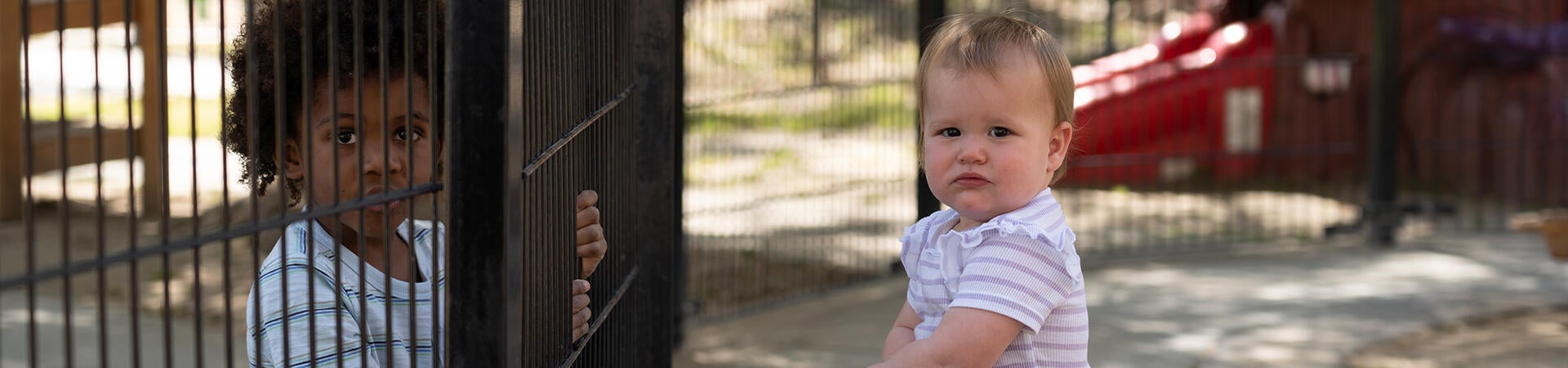 infant looking at older child at fence